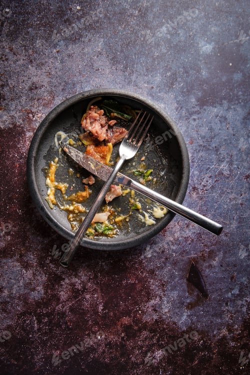 Preview: Fork and knife on black plate with food leftovers