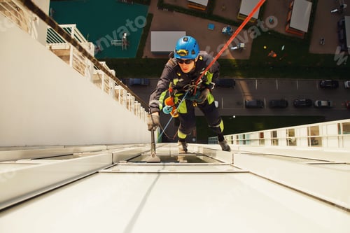 Preview: Industrial mountaineering worker hangs over building while washing exterior facade glazing