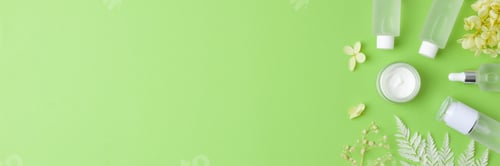 Preview: Cosmetic skin care products with with flowers on green background. Flat lay, copy space