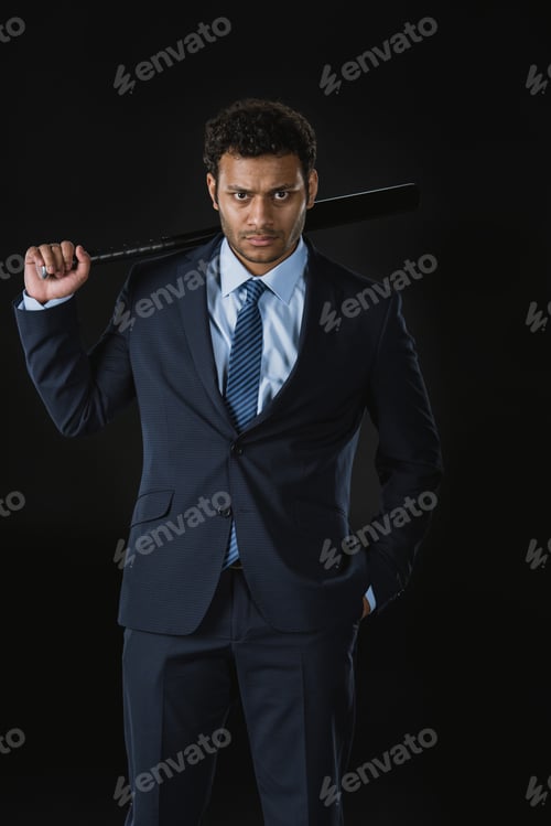 Preview: Confident young businessman with hand in pocket holding baseball bat and looking at camera