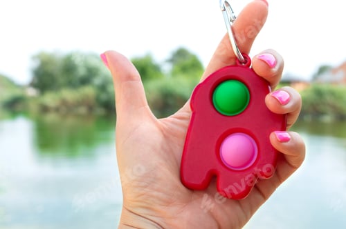 Preview: Simple dimple - colorful rubber antistress trinket toy in the hand. Close-up.