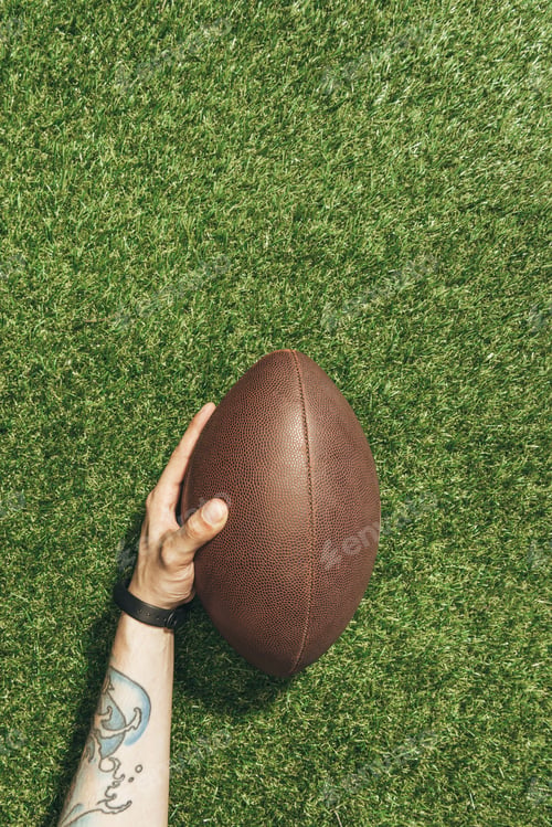 Preview: cropped shot of man holding rugby ball in hand on green lawn background