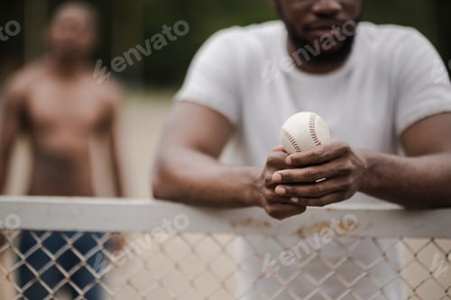 Preview: young handsome man with baseball ball leaning on fence on court