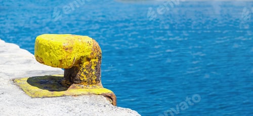 Preview: Yellow rusty port bollard on Greek island harbor pier, blur sea water background, copy space.