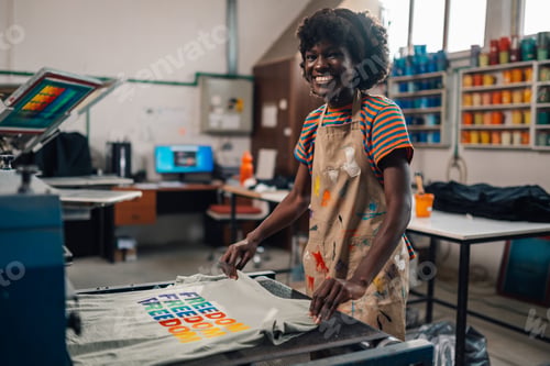 Preview: Happy interracial print shop worker putting t-shirt into drying machine