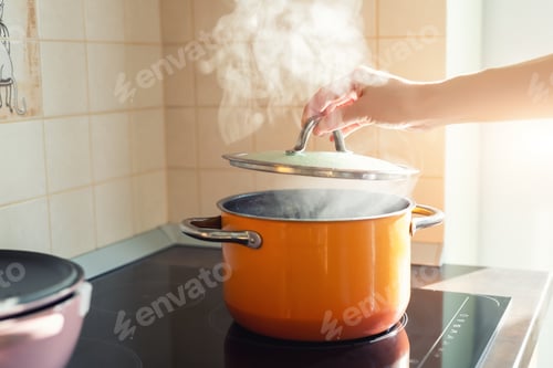Preview: Female hand open lid of enamel steel cooking pan on electric hob with boiling water or soup and