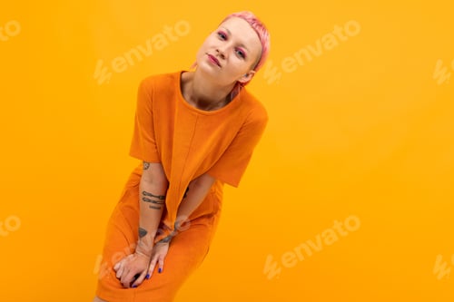 Preview: Unusual pretty woman with short pink hair and tattoo smiles isolated on orange background