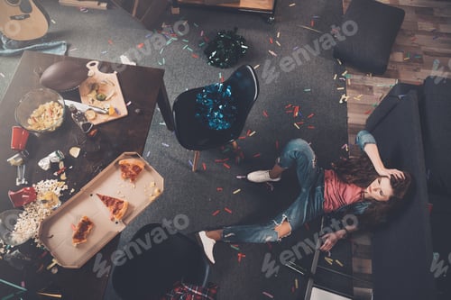 Preview: Top view of young drunk woman lying on floor in messy room
