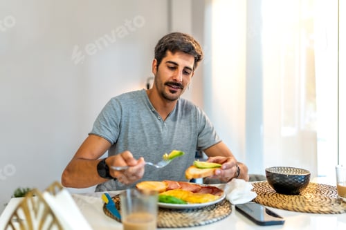 Preview: Young man enjoying healthy breakfast with avocado toast at home