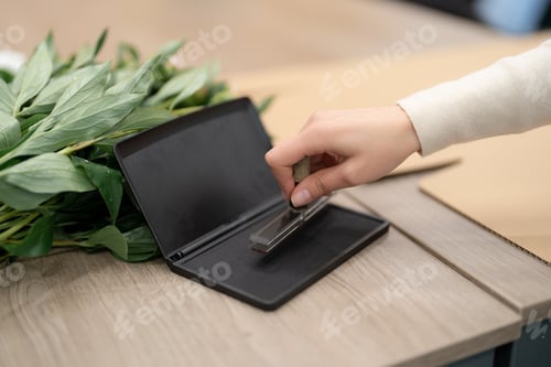 Preview: Woman hand placing a stap on a present box in the shop