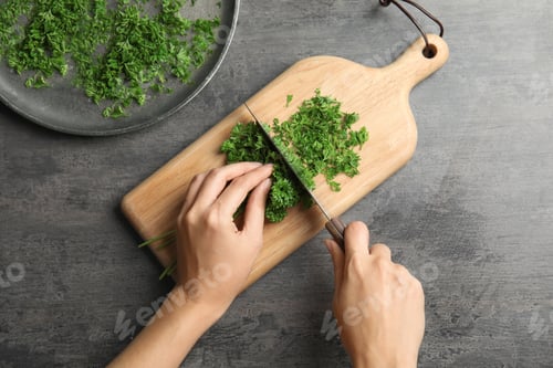 Preview: Woman cutting fresh green parsley on wooden board, top view