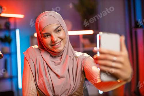 Preview: Adorable woman in hijab using mobile for taking selfie