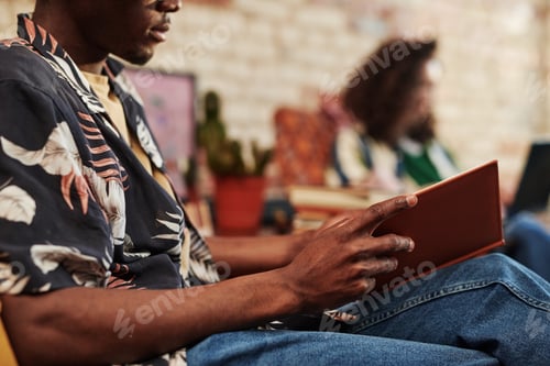 Preview: Hands of young black man in jeans and shirt opening book in hard brown cover