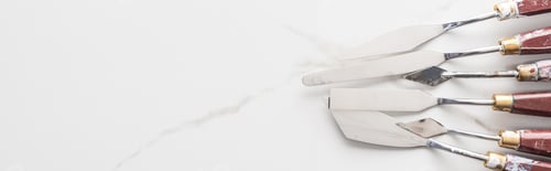 Preview: top view of metal spatulas for drawing on marble white surface with copy space, panoramic shot