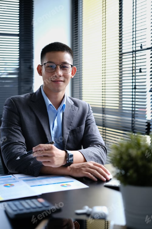 Preview: Portrait of successful businessman in smart suit sitting in modern workplace and looking at camera.
