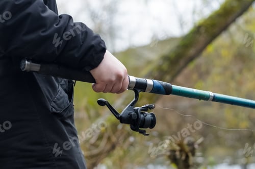 Preview: Man fishing in a wild lake. Male hands are holding a fishing rod, close-up. Autumn fishing in cold