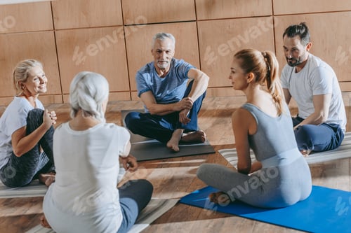 Preview: smiling senior people with instructor sitting on yoga mats at training class