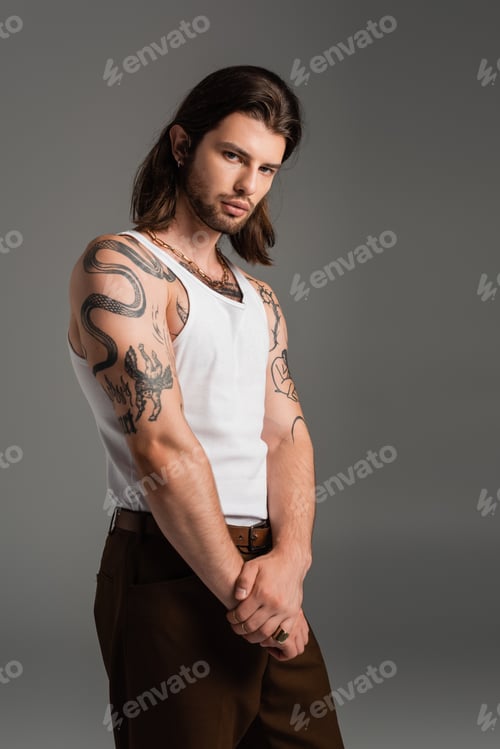 Preview: Stylish tattooed man in white sleeveless short looking at camera isolated on grey