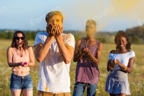 Preview: young multiethnic friends blowing powder from palms at holi festival