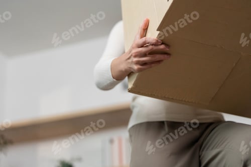 Preview: Moving and Lifting. Close-up of woman lifting a cardboard box during relocation.