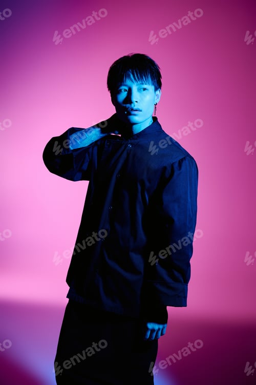 Preview: Stylish asian man poses confidently against a vibrant backdrop of pink and blue hues