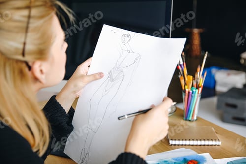 Preview: cropped shot of young fashion designer holding sketch and pen at workplace