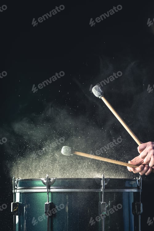 Preview: A man plays a musical percussion instrument with sticks on a dark background.