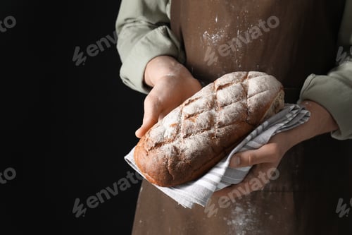 Preview: Woman holding freshly baked bread on black background, closeup. Space for text
