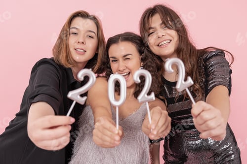 Visualização: Um grupo de garotas está segurando velas dos números 2022 em um fundo rosa.