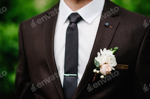 Preview: The groom wiht boutonniere or buttonhole on the jacket, is stands on the background greenery in the