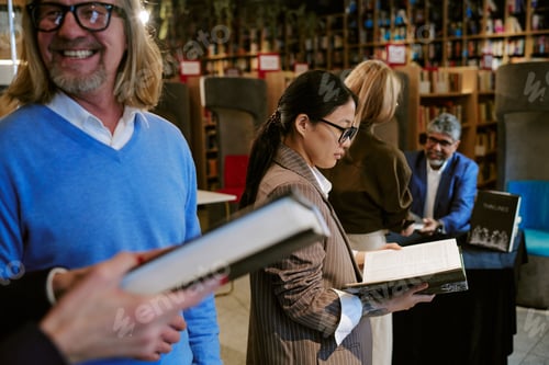 Preview: Young Asian Woman Reading Book during Presentation in Library Surrounded by People