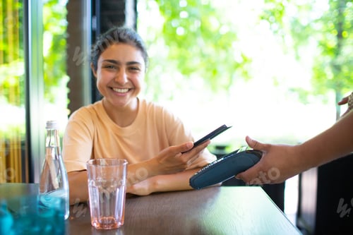 Preview: Indian Woman pay with mobile phone nfc contactless payment terminal in cafe bar