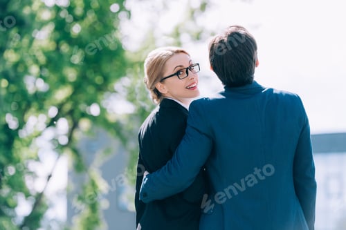 Preview: back view of middle aged business people embracing while standing together on street