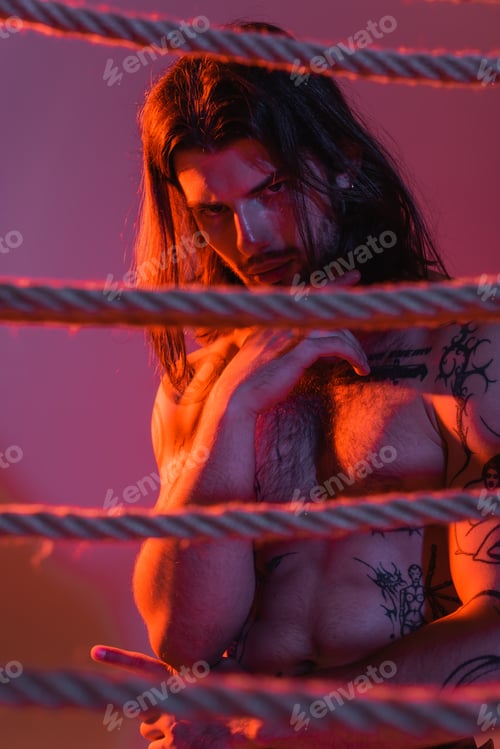 Preview: Sexy tattooed man posing near ropes on purple background with red light
