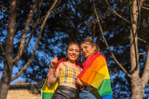 Preview: Two young Caucasian females holding LGBT pride flag outdoors