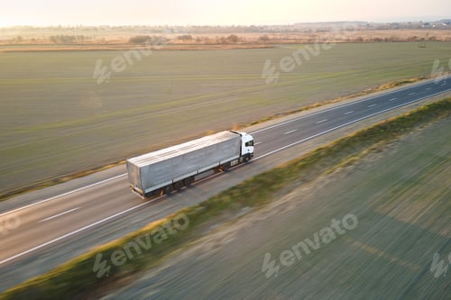 Preview: Aerial view of semi-truck with cargo trailer driving on highway hauling goods in evening.
