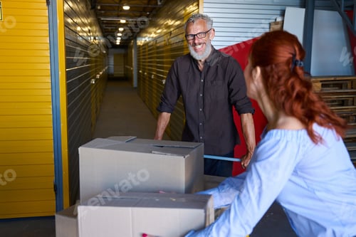 Preview: Smiling man with cargo cart with boxes in warehouse