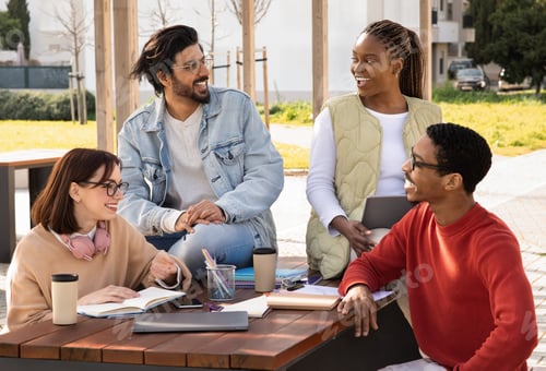 Preview: Cheerful international millennial students study and prepare project together at table with gadgets
