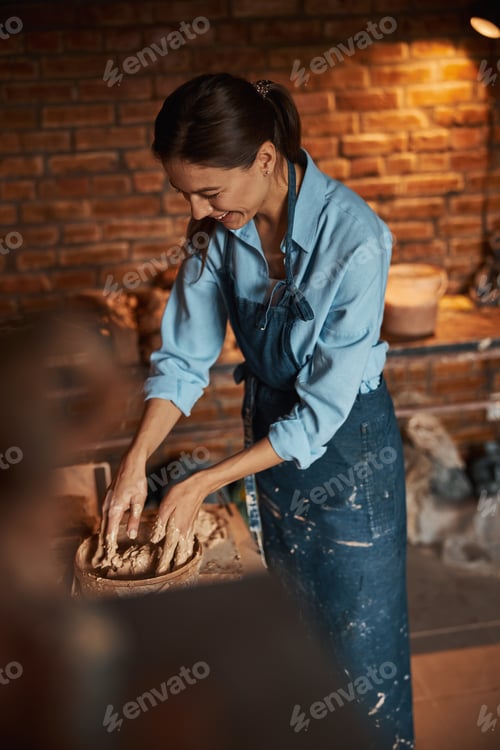 Preview: Charming young Caucasian ceramicist squeezing fresh wet clay in art studio