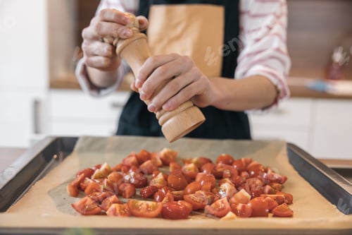 Preview: Hands of a girl grinding pepper on cherry tomatoes using wooden mill