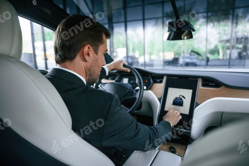 Preview: Rear view. Businessman in suit is driving his electric car