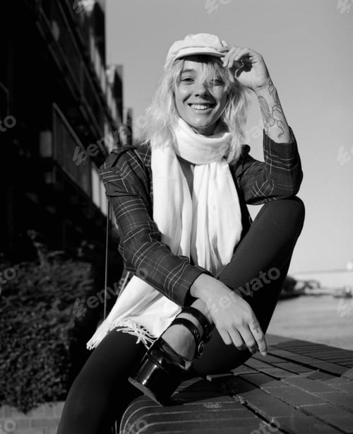 Preview: Smiling alternative female model is looking at camera sitting on stairs outside. Analog film camera.
