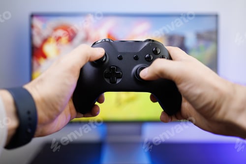 Preview: Hands hold a video game controller in front of the monitor. Video game gamepad in hand
