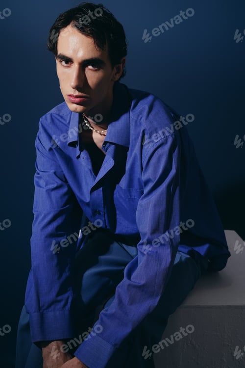Preview: Handsome man in stylish outfit poses against a dramatic blue backdrop, exuding confidence and flair