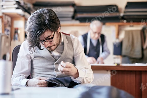 Preview: Tailor with measuring tape around neck working with material at bench