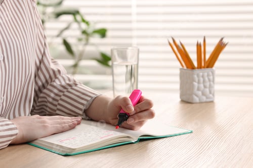 Preview: Woman highlighting important information at wooden desk indoors, closeup