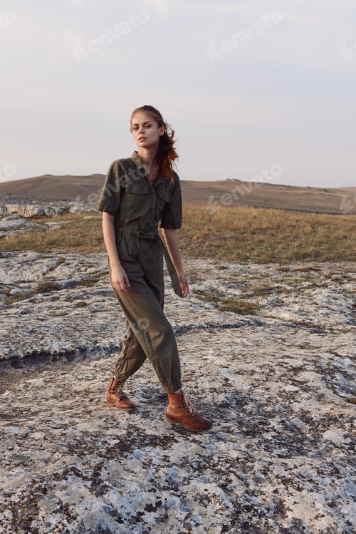 Preview: Woman in olive green jumpsuit standing alone on remote rock formation in desert landscape