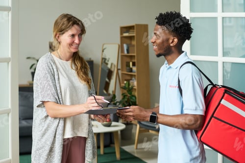 Preview: Woman Signing for Food Delivery from Black Man Courier Indoors