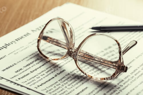Preview: Clear glasses resting on an employment contract with a pen beside it