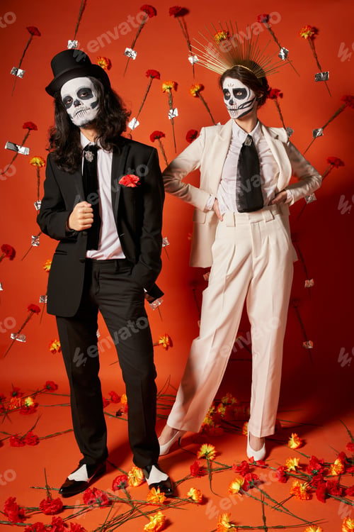 Preview: dia de los muertos party, couple in skeleton makeup and festive attire in red studio with carnations